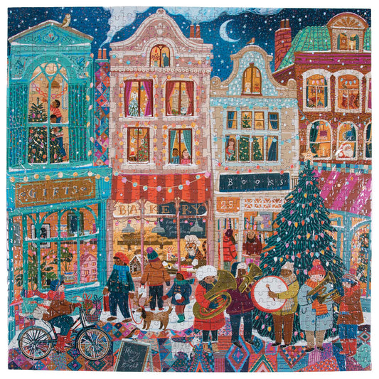 Piece & Love Happy Holidays Festive Puzzle showing a colorful winter street scene with decorated buildings, shopfronts, Christmas tree, and people celebrating