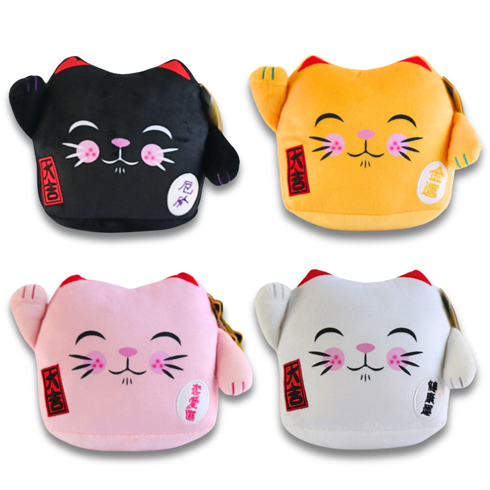 Four plush Maneki Neko lucky cat cushions in black, gold, pink, and white with closed eyes, pink cheeks, raised paws, and red tags
