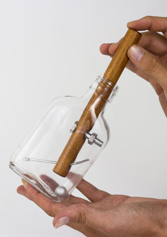 Modeled by a child: wooden-handled glass bottle puzzle with metal internal mechanism, held in two hands against plain background