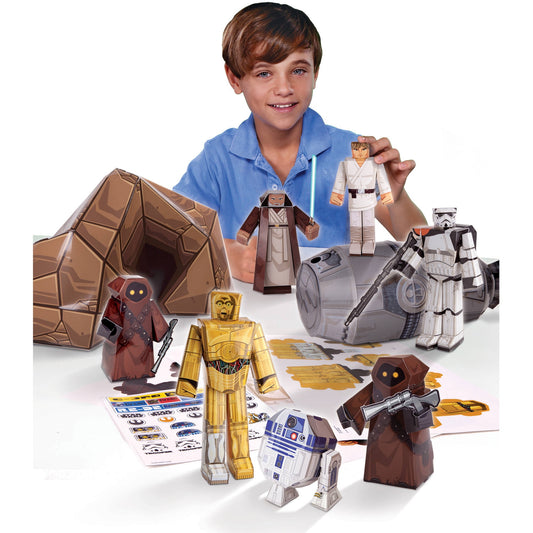 Child modeled by a boy in blue shirt displaying Star Wars Tatooine Droid Builder paper craft kit with assembled cardboard figures including C-3PO, R2-D2, Jedi,