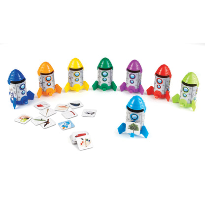 Seven colorful toy rockets with colored domes in blue, orange, yellow, green, purple, red, and lime green, each with gray bodies and circular windows, arranged