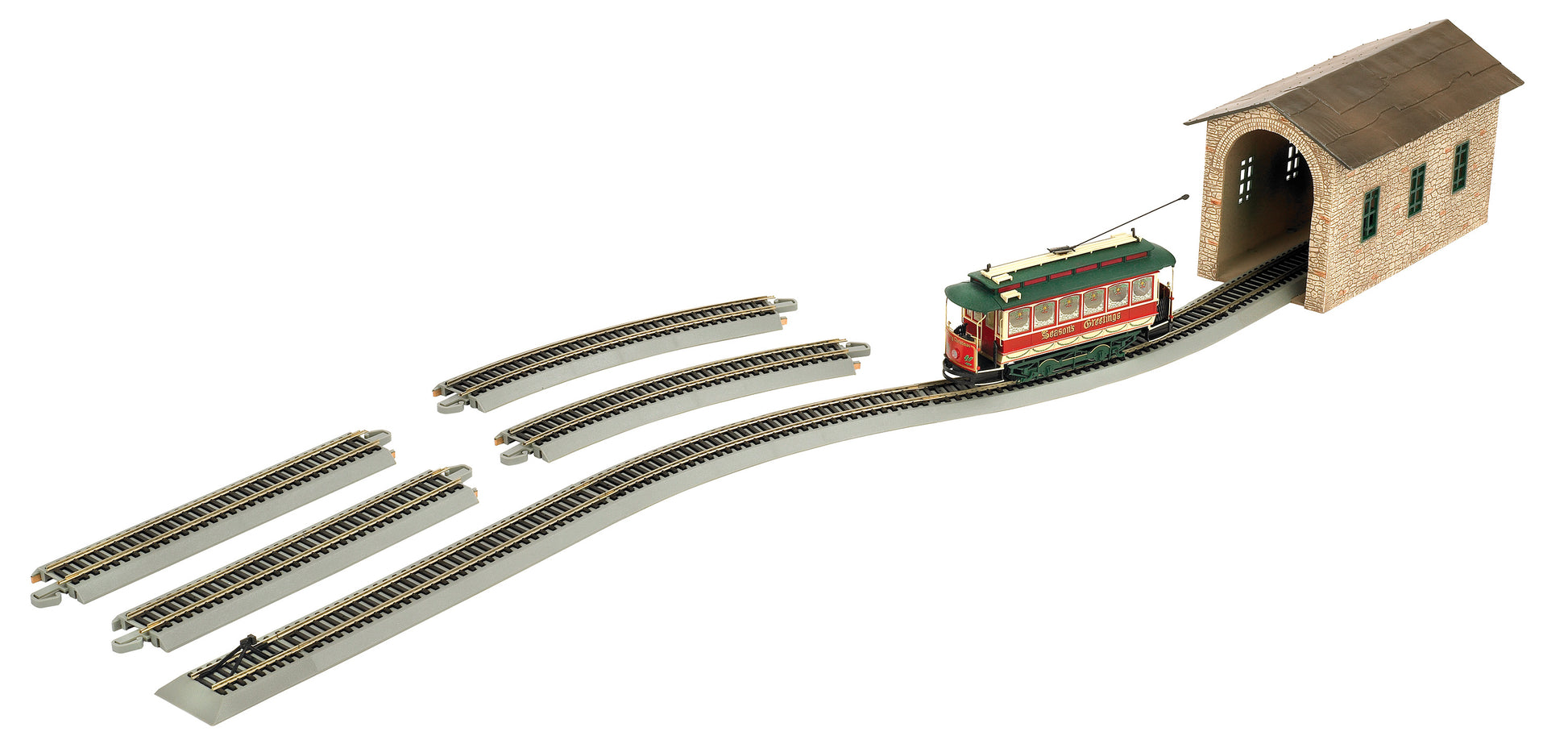 Model train set with red and green streetcar, curved and straight track sections, and brick depot building with arched entrance