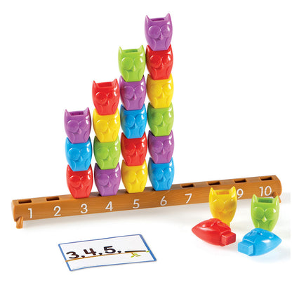 Colorful stacking owl cups in rainbow colors arranged on a numbered wooden ruler from 1-10, with activity cards and owl-shaped counters displayed below
