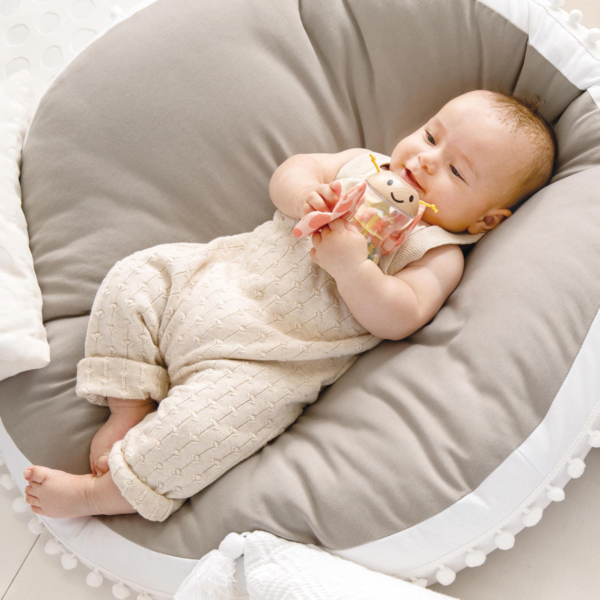 Butterfly Rainmaker Robert soft toy in pink held by baby in beige outfit