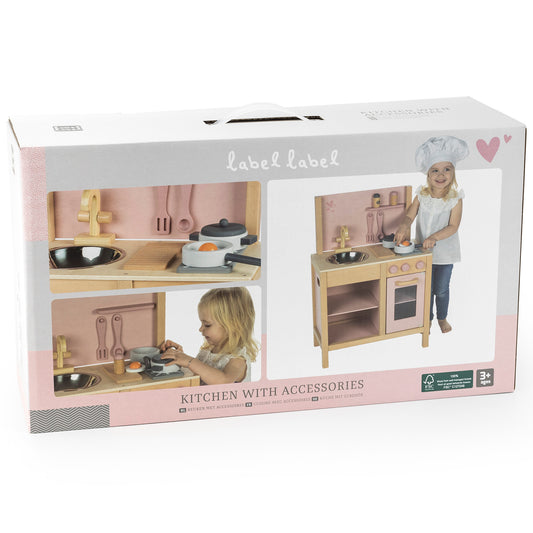 Label Label wooden play kitchen with pink and natural wood finish, includes stove, oven, sink, and metal cooking accessories, shown on packaging with child mode