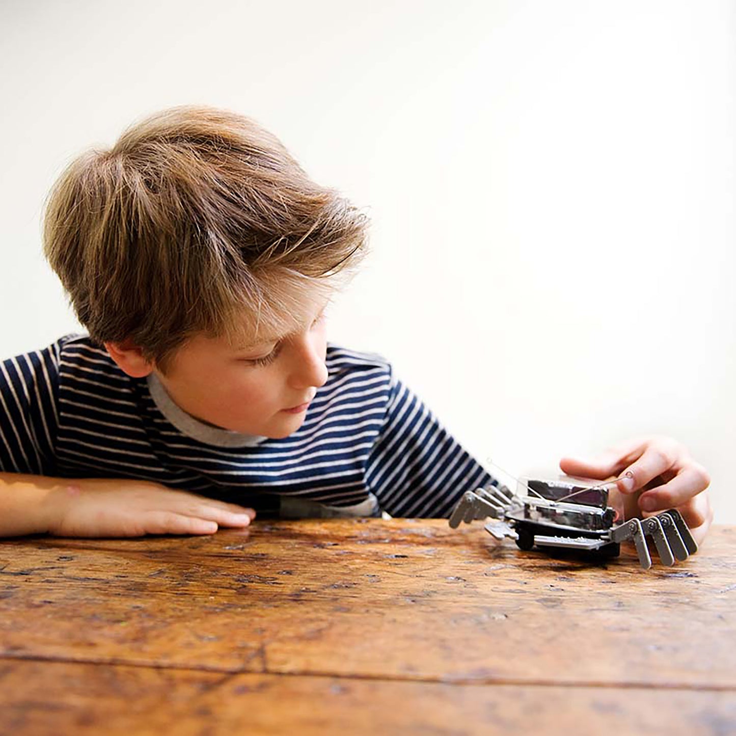 Boy playing with KidzRobotix Table Top Robot toy on wooden surface