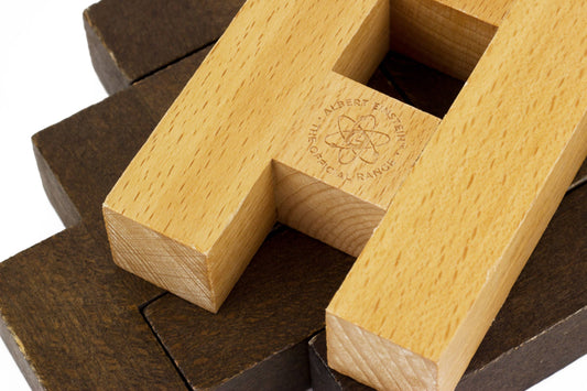Wooden letter blocks in light and dark wood tones assembled to spell a word, with Albert Einstein logo and text engraved on one block, displayed on dark wood su