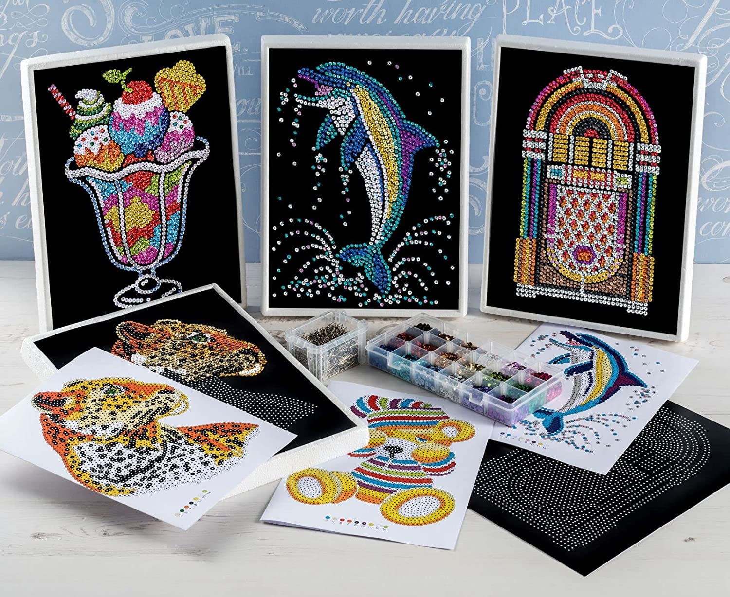 Sequin Art craft kit display showing completed colorful sequin designs including ice cream, dolphin, jukebox, fish, and llama, with instruction sheets, color-co
