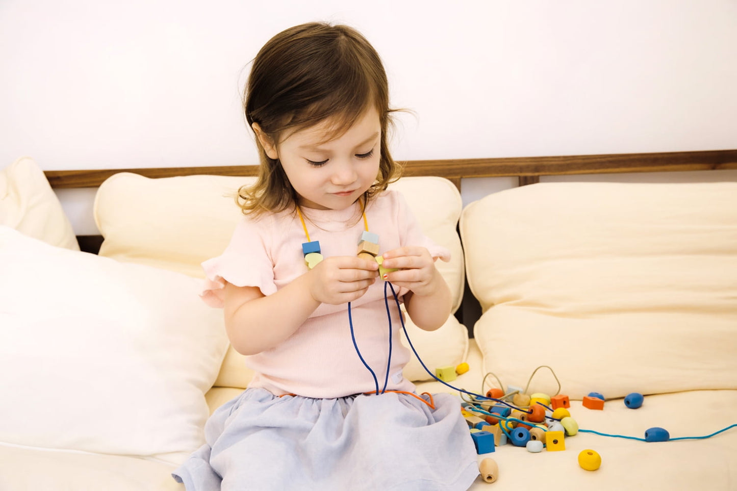 Toddler on model playing with colorful wooden beads and lacing strings on a cream sofa