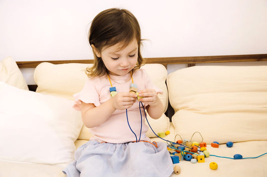 Toddler on model playing with colorful wooden beads and lacing strings on a cream sofa