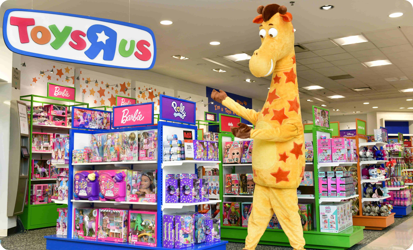 Geoffrey the Giraffe pointing at Toys R Us sign in store