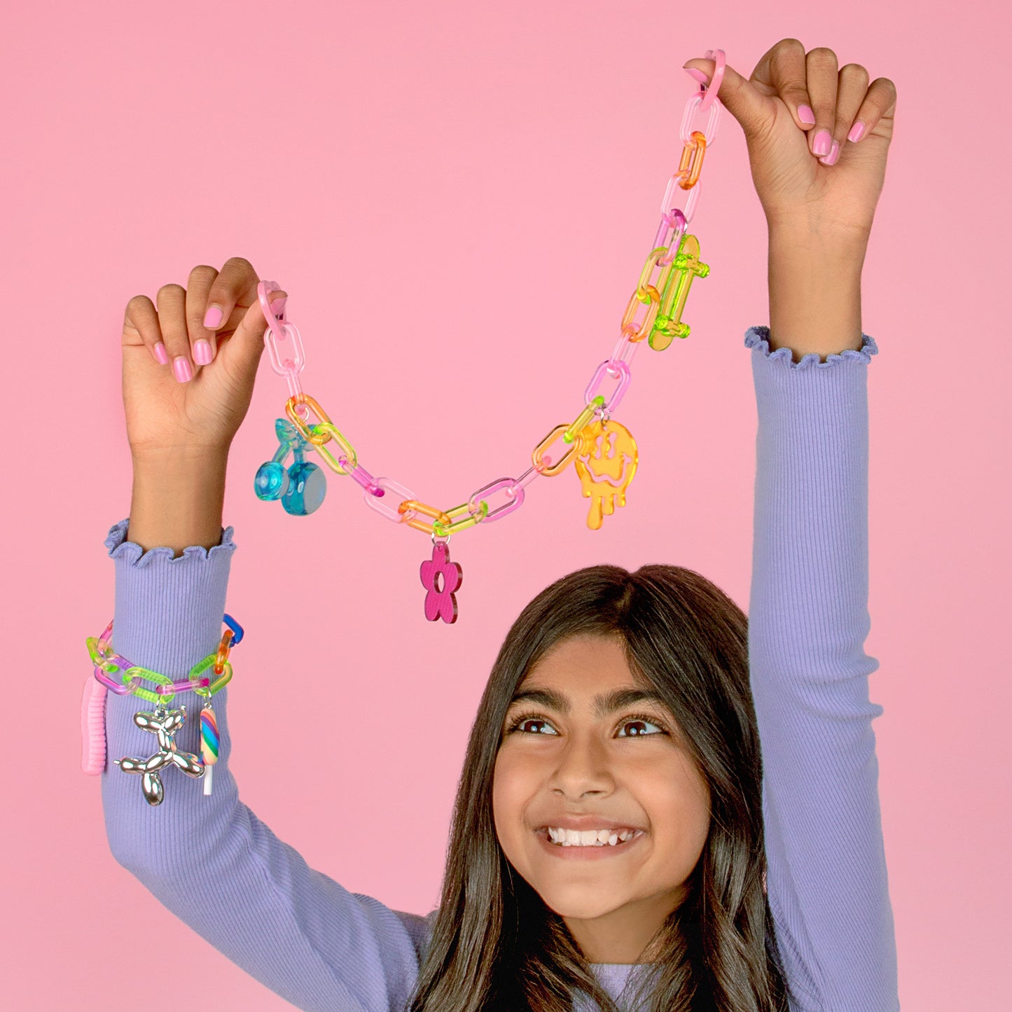 Girl wearing purple sleeves holding colorful Chunky Charms & Chains: So Rad chain necklace with pink and yellow charms