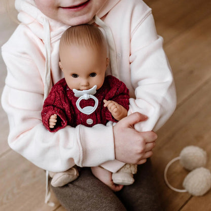 Jubilee Sleepy Aquini 13-inch doll in red outfit with white pacifier, held by child