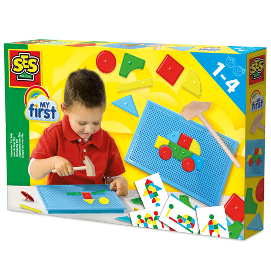 Modeled by a child in red shirt using SES Creative My First Hammer Tap Tap toy with blue pegboard, colorful shapes, wooden hammer, and instruction cards showing