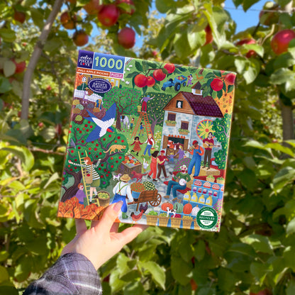 eeBoo Fall Apple Picking 1000 Piece Jigsaw Puzzle held in hand against apple orchard background