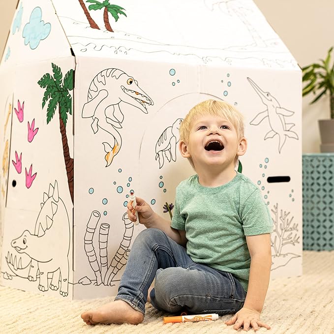 Child sitting inside a cardboard dinosaur playhouse with illustrated dinosaurs and jungle scene, modeled by a child in green shirt