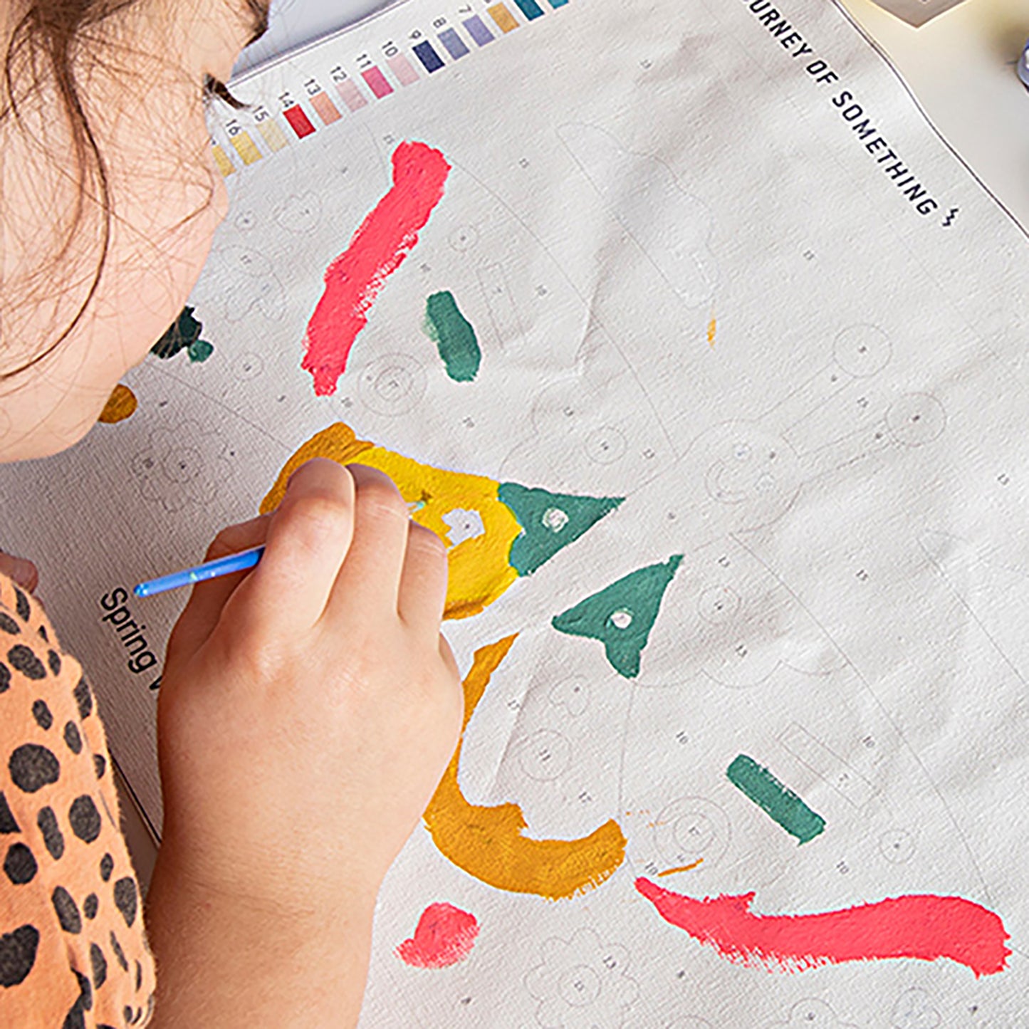 Child painting JOS Paint By Numbers Outside The City with blue brush on colorful map