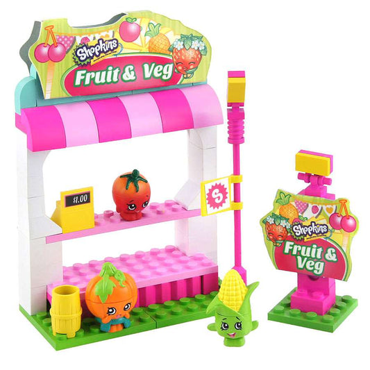 Shopkins Fruit & Veg Stand building set with pink and white market stall, striped awning, colorful fruit and vegetable character pieces, and scale sign