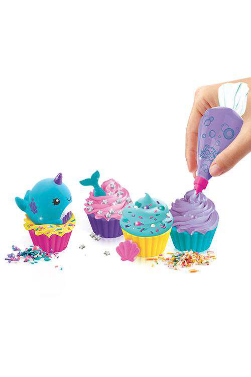 Hand squeezing purple soap frosting from bottle onto colorful cupcake-shaped soap molds with dolphin and shell decorations