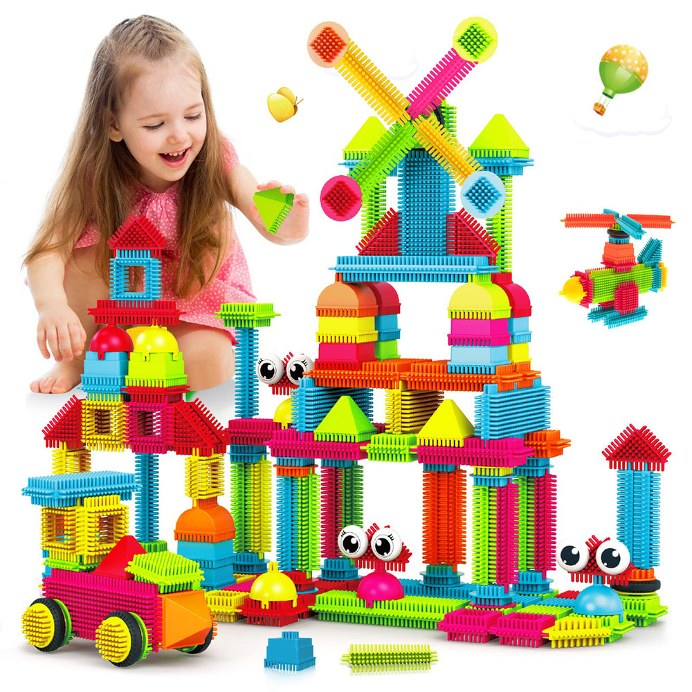 Child modeled playing with colorful bristle building blocks assembled into a multi-story castle structure with towers, domes, and decorative shapes in red, yell
