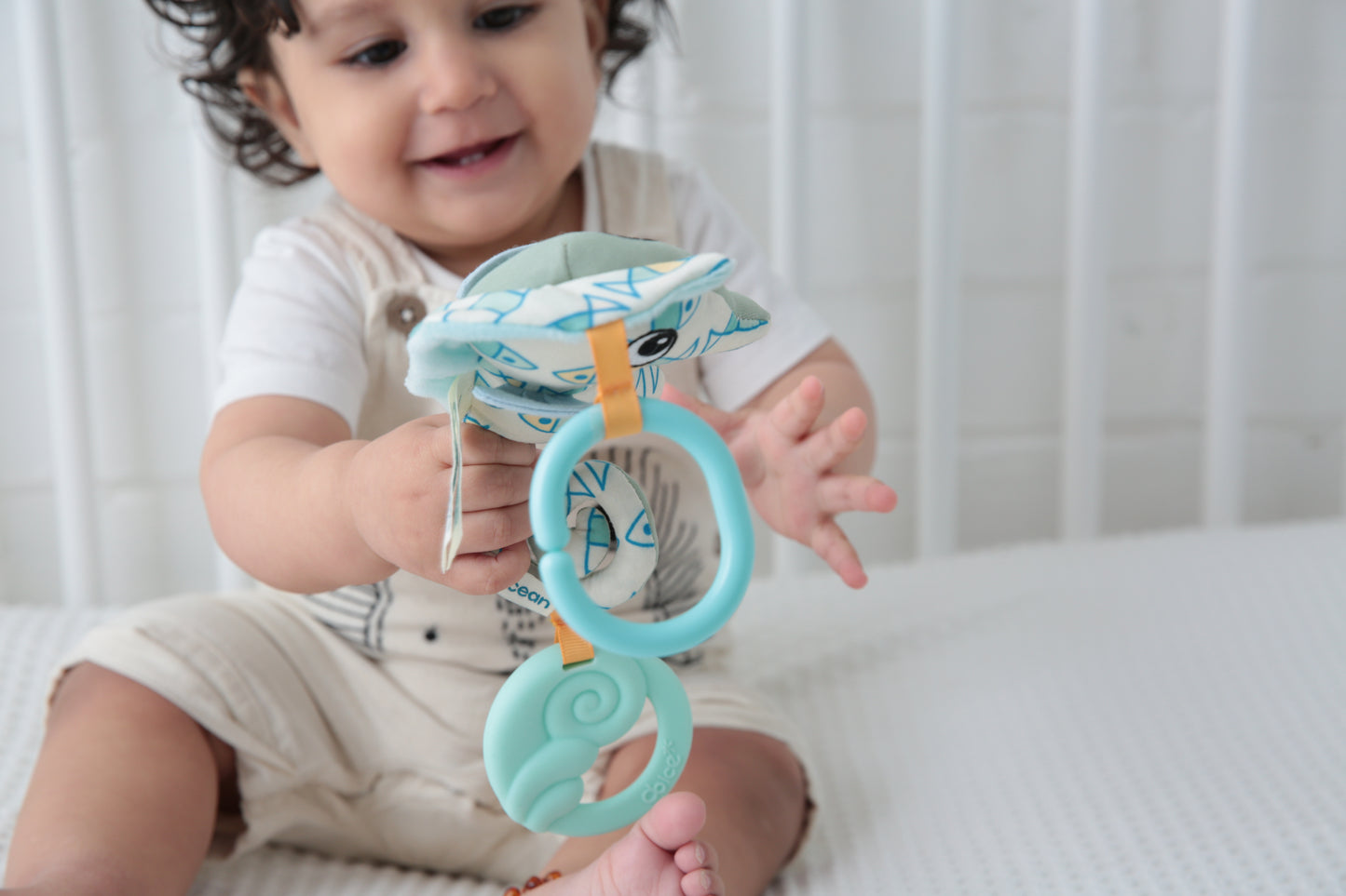Toddler holding blue seahorse-shaped teether toy with textured rings, modeled by a child