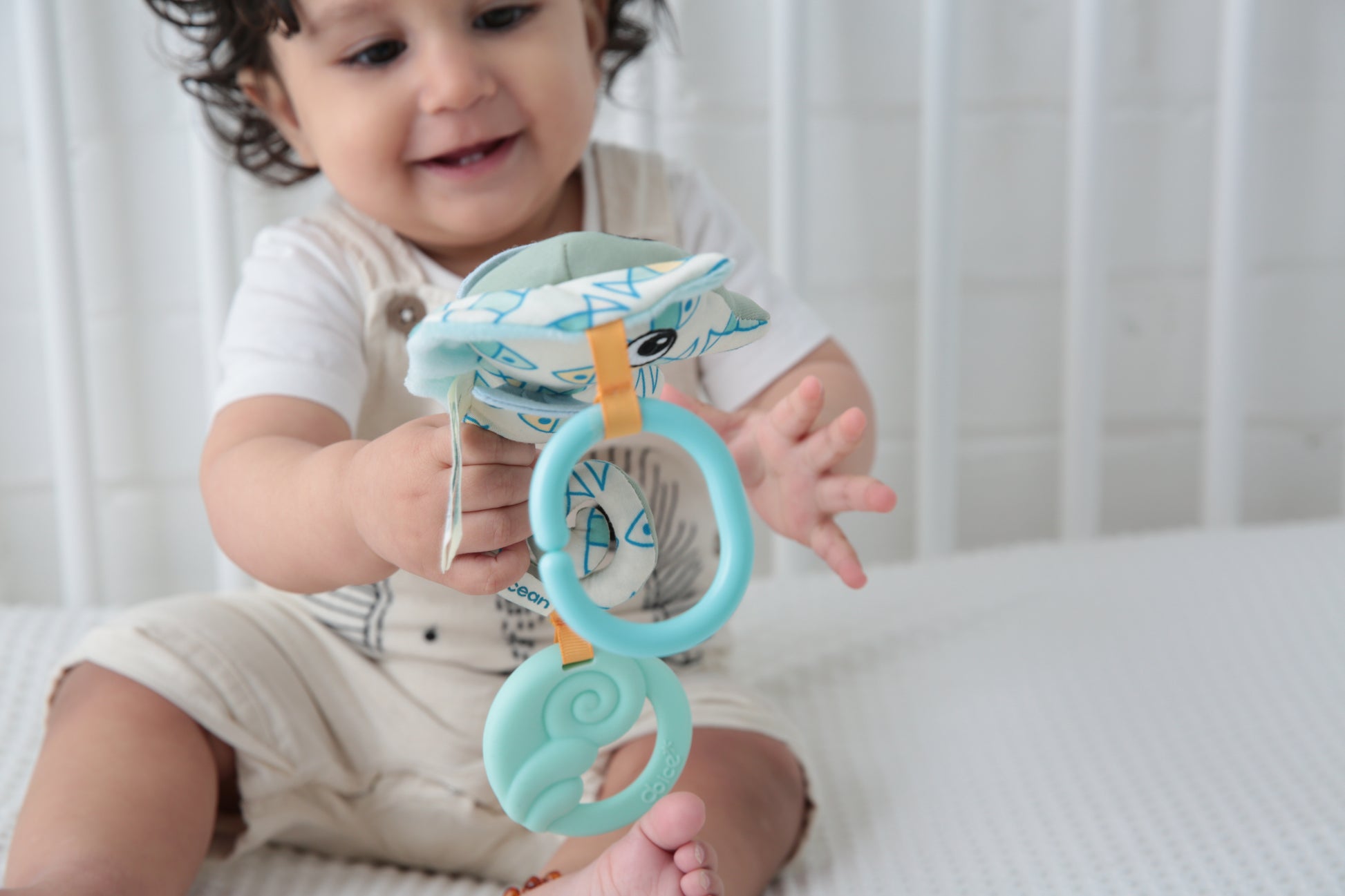 Toddler holding blue seahorse-shaped teether toy with textured rings, modeled by a child