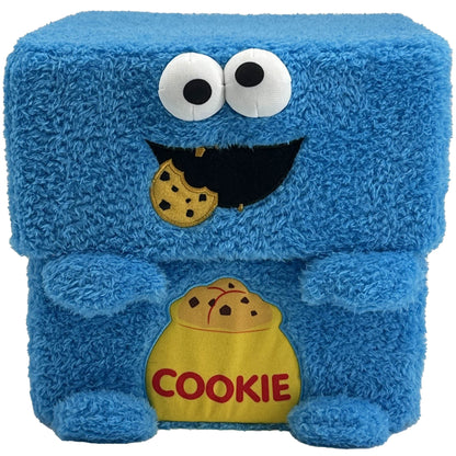Blue plush cube storage bin with Cookie Monster face, white eyes with black pupils, open mouth smile, and yellow cookie pouch pocket labeled COOKIE