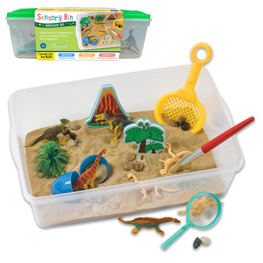 Creativity for Kids Sensory Bin Dinosaur Dig set with clear plastic container filled with sand, dinosaur figures, volcano and plant scenery pieces, yellow scoop