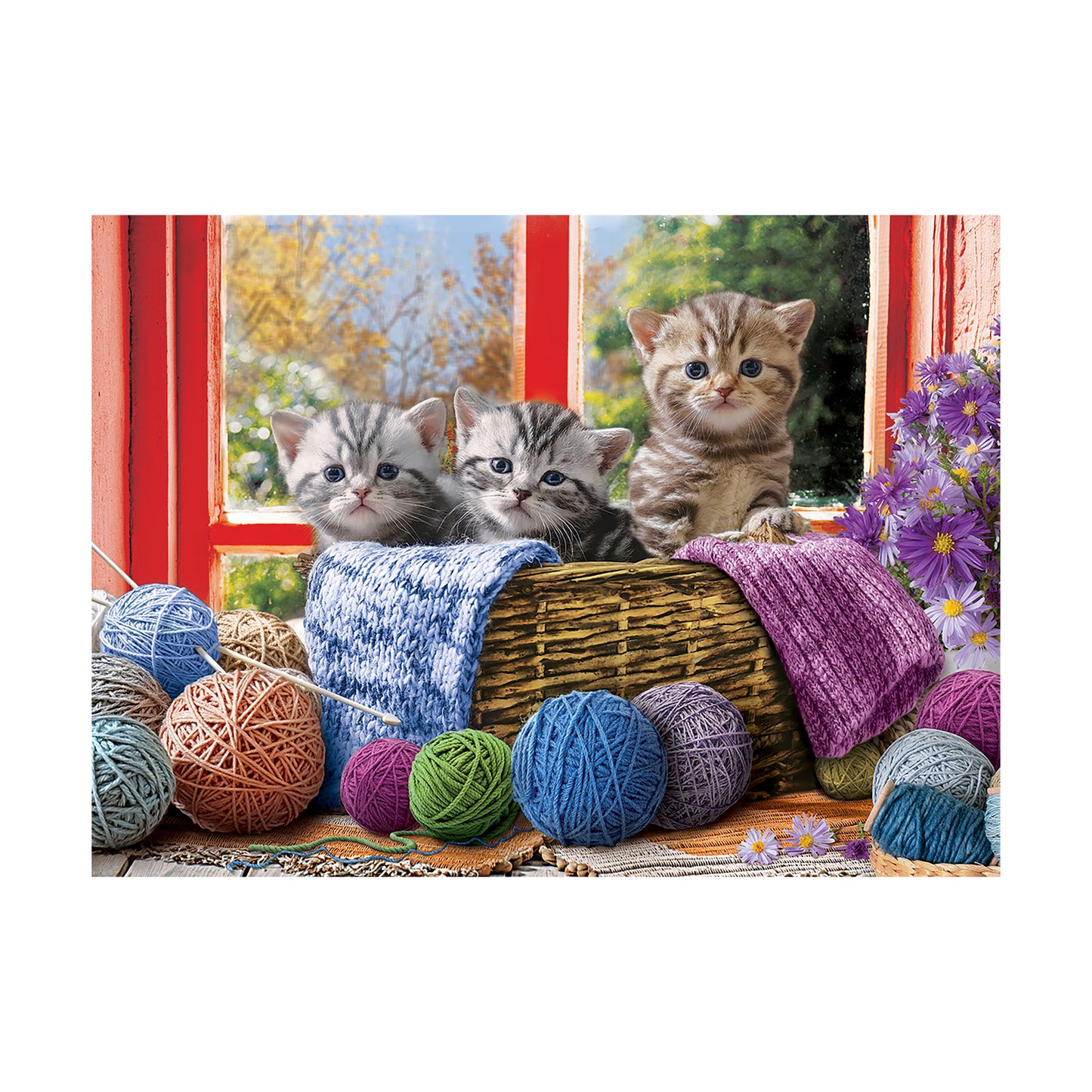 Three tabby kittens looking out a red window beside a wicker basket with colorful yarn balls and knitted blankets, purple flowers visible on right side