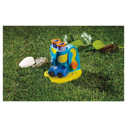 GeoSafari Jr. STEM Microscope with blue and yellow body, orange eyepieces, and LED light on grass