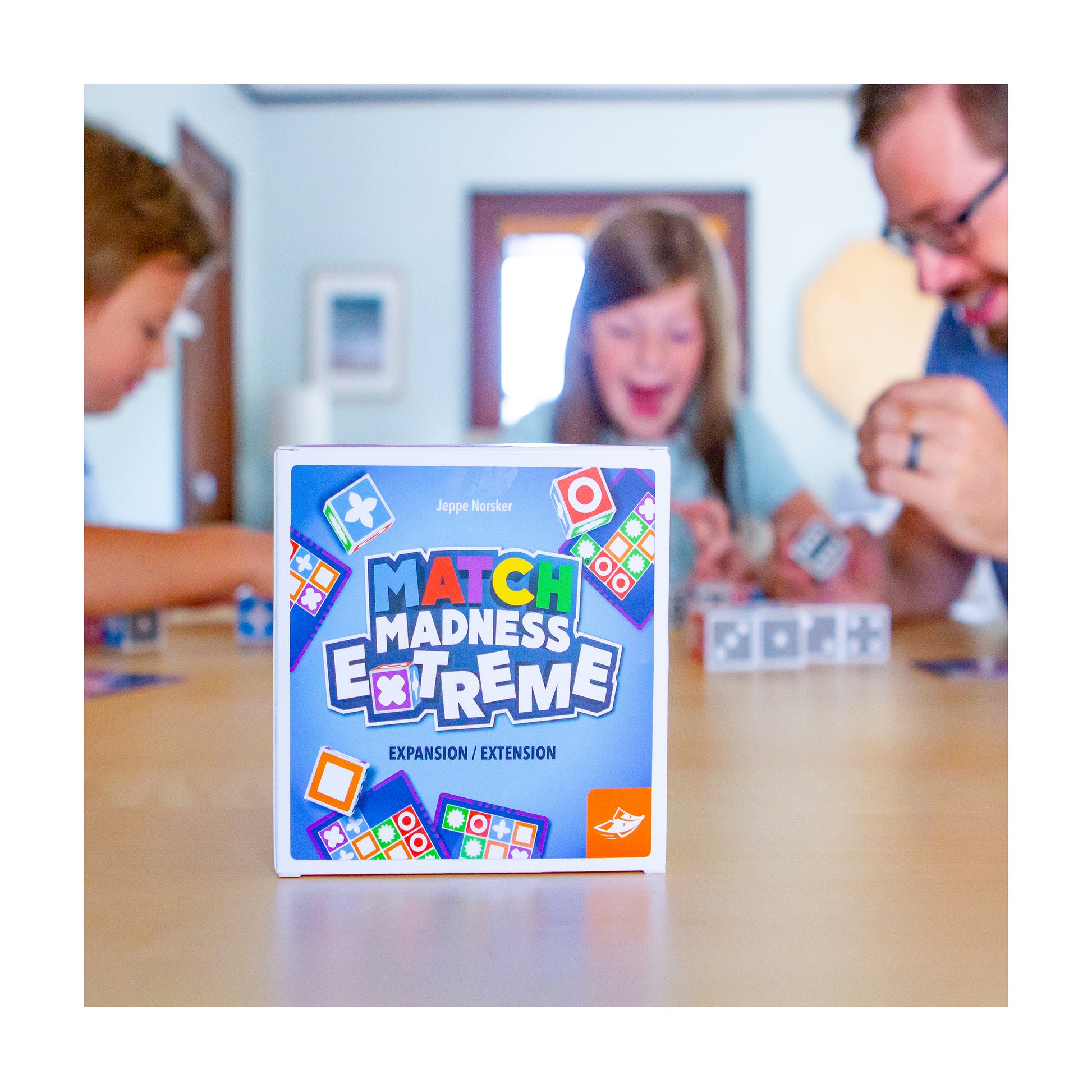 Match Madness Extreme Expansion game box with colorful tiles, displayed on table with children playing in background
