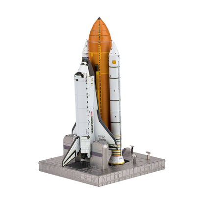 Metal Earth ICONX 3D Space Shuttle Launch model kit assembled and displayed on gray launch pad base, showing white orbiter with orange fuel tank and boosters
