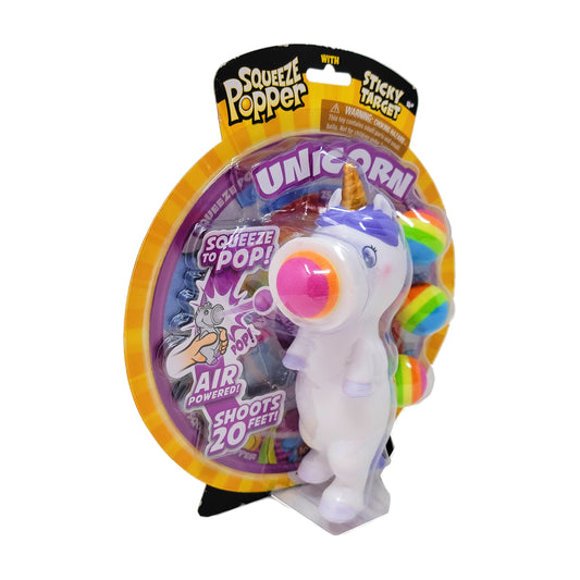 White unicorn squeeze popper toy with pink eye, gold horn, and rainbow mane, shoots sticky targets up to 20 feet, on yellow and purple packaging