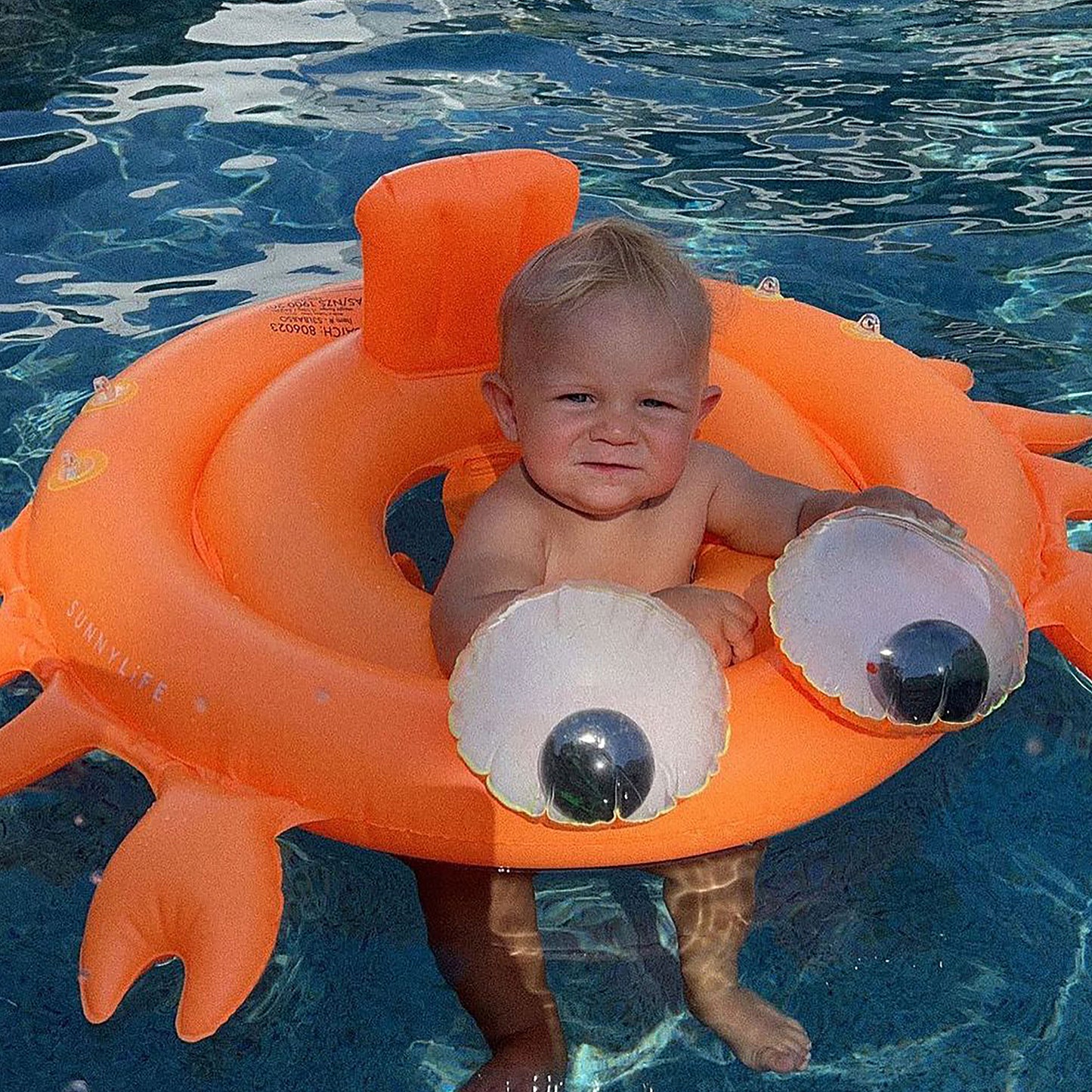 Baby Float Sonny the Sea Creature in neon orange with eye details in pool